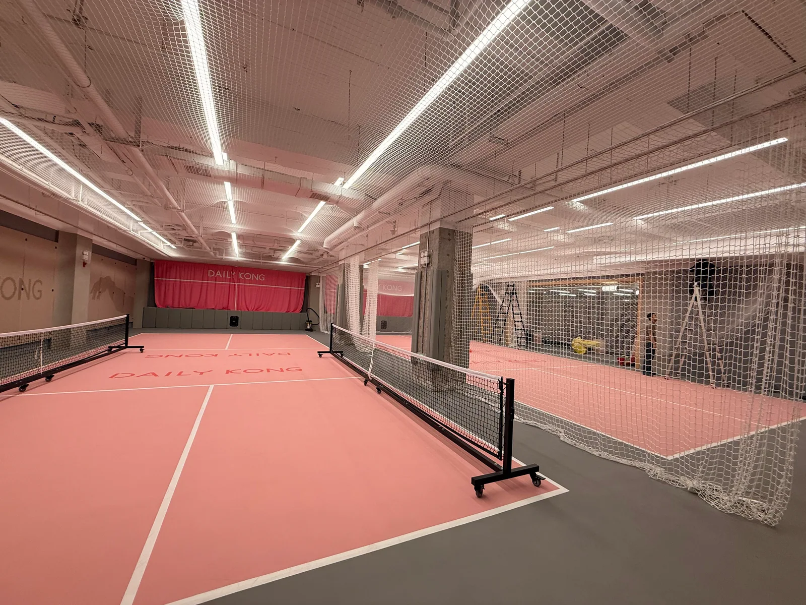 Indoor court with a pink playing surface and perimeter netting